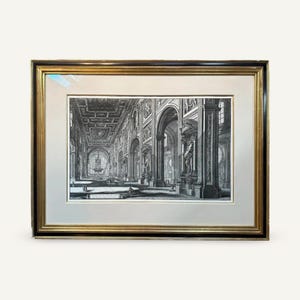 May include: A framed black and white architectural print. The print depicts a long interior space with arches, columns, and statues. The frame is gold and black.