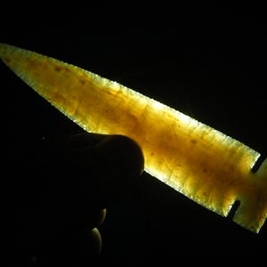 May include: A translucent yellow arrowhead with a pointed tip and a flat base. The arrowhead is made of a smooth, polished material and has a slight curve to it.