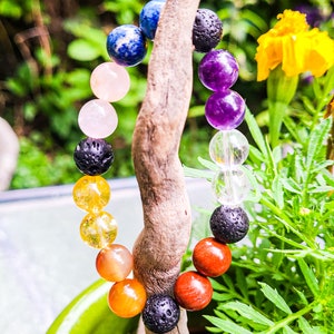 May include: A colorful beaded bracelet with seven different colored beads, including blue, pink, yellow, orange, red, purple, and black. The bracelet is made of natural stones and is strung on a stretchy cord.