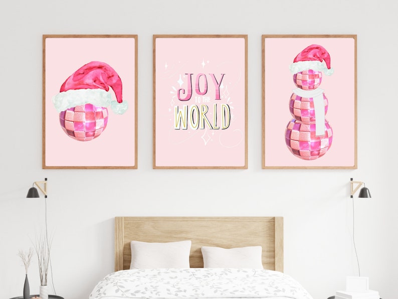 May include: Three pink and white Christmas-themed prints with a disco ball theme. The first print features a disco ball wearing a Santa hat. The second print says "Joy to the World" in a pink and gold font. The third print features a snowman made of disco balls wearing a Santa hat and a white scarf.