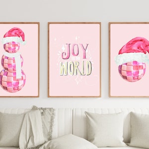 May include: Three pink framed prints with a pink disco ball snowman, a pink disco ball with a Santa hat, and a pink background with the text "Joy to the World" in gold letters.