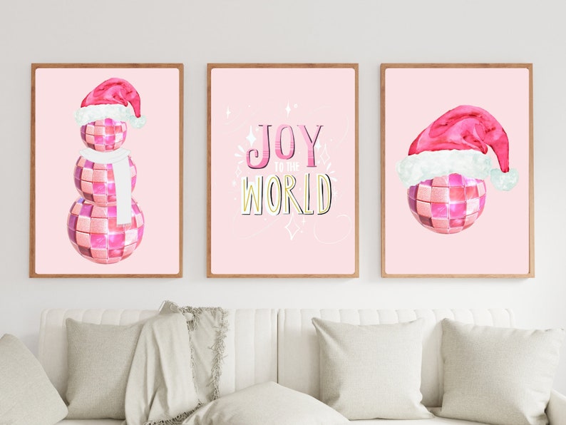 May include: Three pink framed prints with a pink disco ball snowman, a pink disco ball with a Santa hat, and a pink background with the text "Joy to the World" in gold letters.
