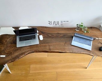 Può includere: Una grande scrivania in legno con bordo vivo e un fiume di resina epossidica bianca che attraversa il centro. Due laptop sono sulla scrivania, uno su ciascun lato del fiume. La scrivania è sostenuta da gambe a forcina. La scrivania è realizzata da Ri/Ui - Tables Design.