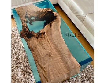May include: A large, wooden coffee table with a turquoise epoxy resin inlay. The table has a natural wood grain and a unique shape. The text "RIVULET tables design" is visible on the table.