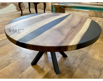 Op de afbeelding: Een ronde houten salontafel met een zwarte epoxyhars inlay. De tafel heeft een zwart metalen onderstel met vier poten.