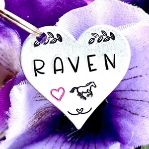 May include: Silver heart-shaped tag with the name "RAVEN" engraved in black lettering. A small pink heart and a black silhouette of a horse are also engraved on the tag.