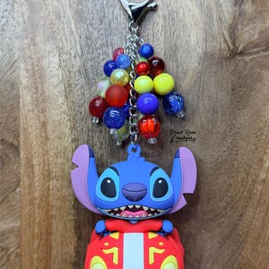 Puede incluir: Un llavero de Stitch azul con un coche rojo, sujeto a una cadena y cierre plateados. El llavero tiene un grupo de cuentas de colores rojo, amarillo, azul y transparente. El texto "Briar Rose Creations" es visible.
