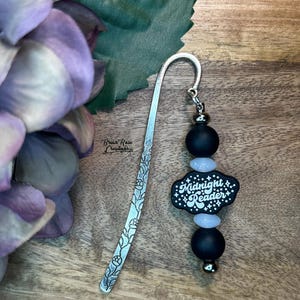 May include: A silver bookmark with a floral design and a black and white beaded charm that says "Midnight Reader".