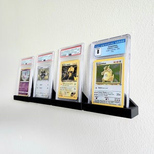 Puede incluir: Cuatro cartas de intercambio de Pokemon se muestran en estuches protectores en un soporte de pared. Las cartas est&aacute;n clasificadas por CGC Universal Grade y presentan a Kangaskhan, Rocket's Zapdos y otros dos Pokemon. Las cartas est&aacute;n en excelente estado y tienen una calificaci&oacute;n alta.