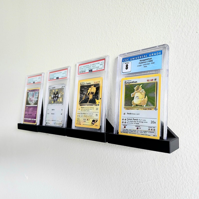 Puede incluir: Cuatro cartas de intercambio de Pokemon se muestran en estuches protectores en un soporte de pared. Las cartas est&aacute;n clasificadas por CGC Universal Grade y presentan a Kangaskhan, Rocket's Zapdos y otros dos Pokemon. Las cartas est&aacute;n en excelente estado y tienen una calificaci&oacute;n alta.