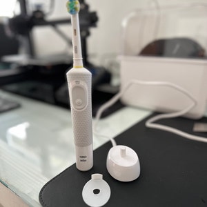 May include: A white electric toothbrush with a gray textured handle and a blue and green brush head. The toothbrush is on a white charging base with a white cord.
