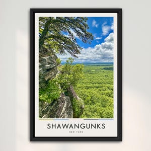 May include: Framed print of a scenic landscape featuring a cliffside view of a lush green forest under a bright blue sky with fluffy white clouds. The print includes the text "SHAWANGUNKS NEW YORK" at the bottom.