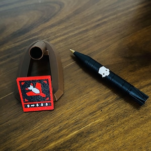 May include: A brown plastic display stand with a red square warning sign that says "Danger!" and a black and white skull graphic. A black pen with a white skull graphic is lying on a wooden surface.