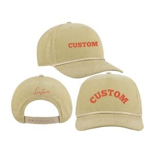 Op de afbeelding: Drie beige corduroy baseballpetten met een touwversiering. Eén pet heeft het woord "CUSTOM" in oranje geborduurd op de voorkant. Een andere pet heeft het woord "Custom" in rood geborduurd op de achterkant. De derde pet heeft het woord "CUSTOM" in oranje geborduurd in een boog op de voorkant.