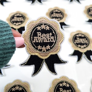 May include: Gold embroidered iron-on patch with a black ribbon and the text "Best Award" in a circle.