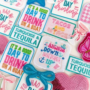 May include: A collection of embroidered and sequined patches featuring various designs including a blue star, a pink heart, cocktail glasses, and text such as "It's a good day to drink on a boat," "You had me at day drinking," "Tacos and margs," and "Anchor down bottoms up."