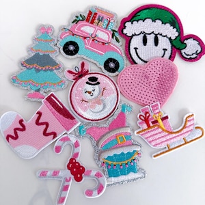 May include: A collection of embroidered holiday patches including a pink car with gifts, a Christmas tree, a snowman ornament, a smiley face in a green hat, a pink sequined heart, a pink stocking, a candy cane, a sleigh, and a chimney with a hat.