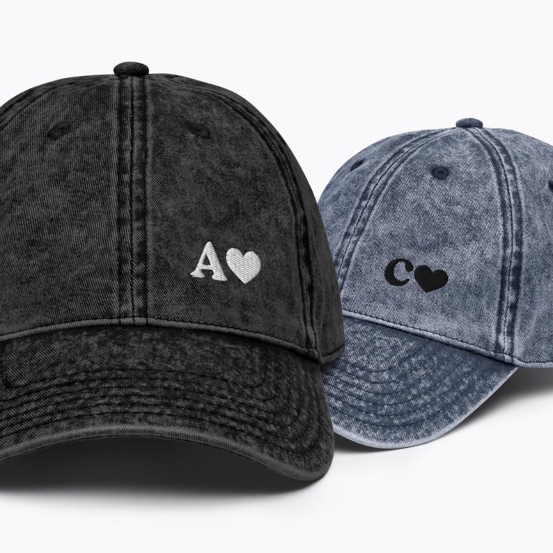 May include: Two denim baseball caps with embroidered letters and hearts. The black cap has a white "A" and heart, and the blue cap has a black "C" and heart.