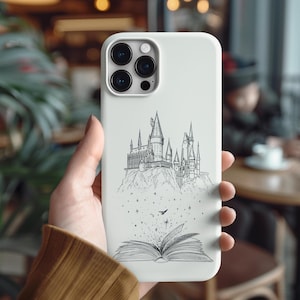 May include: A light gray phone case featuring a black and white illustration of a castle atop a mountain, with an open book at the bottom. A small bird flies above the book. The case has a glossy finish.