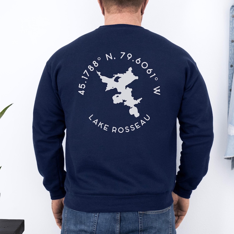 May include: Navy blue sweatshirt with a white graphic of Lake Rosseau, including coordinates and the lake's name. The design is circular and centered on the back of the sweatshirt. The sweatshirt is a solid color.