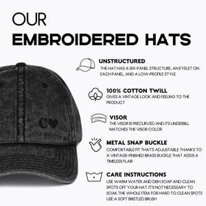 May include: A black distressed baseball cap with a white heart and the letter C embroidered on the front. The cap is unstructured, made of 100% cotton twill, and has a precurved visor. It features a metal snap buckle for adjustability.