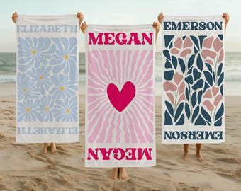 May include: Three beach towels with personalized names, "Elizabeth", "Megan", and "Emerson". Each towel features a different colorful design. The "Megan" towel has a pink and white sunburst design with a red heart in the center. The "Elizabeth" towel has a blue and white floral design. The "Emerson" towel has a blue and pink floral design.