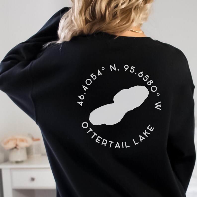 May include: Black sweatshirt with a white graphic of Ottertail Lake, including coordinates 46.4054&deg; N, 95.6580&deg; W. The lake outline and text are in a circular design. The sweatshirt is a casual style.