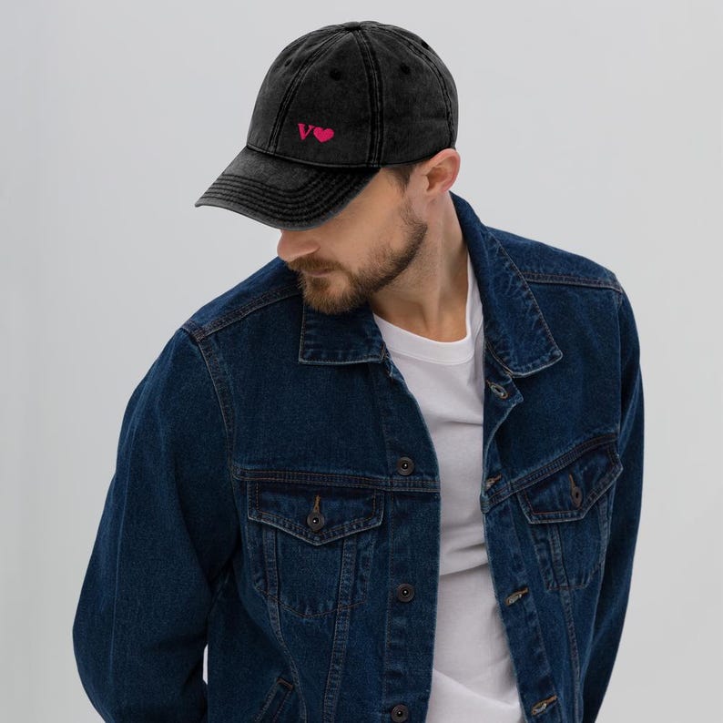 May include: A black distressed denim baseball cap with a pink embroidered heart and the letter "V" on the front.