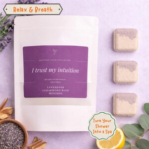 May include: A white pouch with a purple label that reads "I trust my intuition" and "Lavendar & Cedarwood with Menthol." Three square shower steamers with a lavender top layer are to the right. The text "Relax & Breath" and "Turn Your Shower Into a Spa" are also visible.