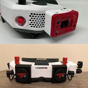 Peut inclure: Lunettes FPV blanches et noires avec le logo HDZero sur le devant, deux capuchons d'antenne rouges et des supports latéraux circulaires noirs avec des graphismes d'oiseaux rouges. L'appareil comprend un module rectangulaire rouge sur le côté.