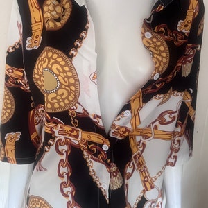 May include: A white and black button-up shirt with a gold chain print. The shirt has a collar and short sleeves.