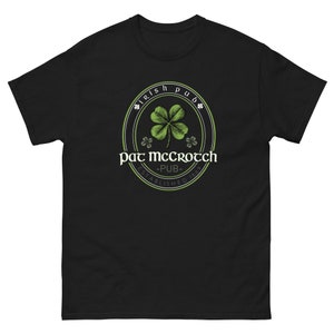 Op de afbeelding: Zwart T-shirt met een groene klaver en de tekst "Irish Pub" en "Pat McGrotch - Pub - Gevestigd in 1869"