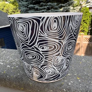 May include: A tapered ceramic planter featuring a high-gloss finish with a black and white hand-painted pattern of concentric, swirling, and irregular circular lines that cover the entire exterior surface of the vessel from top to bottom.
