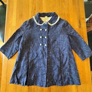 May include: A navy blue coat with a white speckled pattern. The coat has a rounded collar with white lace trim and white buttons. The coat has three-quarter length sleeves and a pleated skirt.