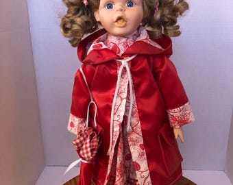 Vintage Girl Doll In Red Raincoat And Dress. Displayed On Stand.