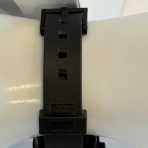 May include: Black watch with a black band. The band is made of a flexible material and has a buckle closure. The watch face is visible at the bottom of the image.