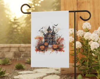 Op de afbeelding: Een witte Halloween-tuinvlag met een aquarel illustratie van een spookhuis, pompoenen en vleermuizen. De vlag wordt getoond op een zwarte metalen tuinpaal, ideaal voor seizoensgebonden buitendecoratie.