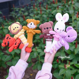 以下が含まれることがあります： 手作りのかぎ針編み動物のおもちゃのコレクション。トラ、ライオン、クマ、ウサギ、紫色の生き物が含まれています。おもちゃはオレンジ、黄色、茶色、白、紫などの様々な色です。画像には「English PDF pattern」というテキストが含まれています。