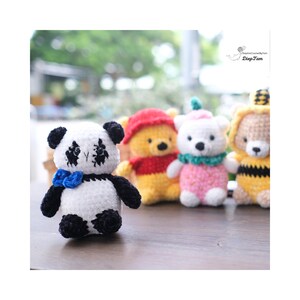 May include: Five crocheted stuffed animals, including a panda, a bear, a polar bear, and two bees. The panda is black and white with a blue bow tie. The bear is yellow with a red shirt. The polar bear is white with a pink dress and a green scarf. The bees are yellow and black with black and white stripes.