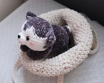 May include: A handmade plush husky dog in a cream-colored crocheted basket. The husky has a gray and white color scheme with black eyes and a pink nose. The basket has a thick, textured appearance.