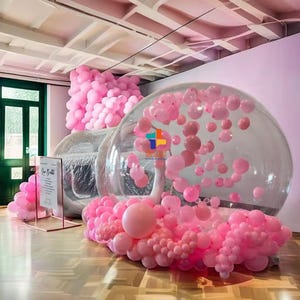 Pode incluir: Uma grande bolha inflável transparente com balões cor-de-rosa dentro. A bolha é cercada por um grande grupo de balões cor-de-rosa.