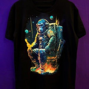 May include: Black t-shirt with a graphic print of a chimpanzee wearing a spacesuit and headphones, sitting in a chair with flames underneath. The chimpanzee is in a space setting with planets and stars in the background.