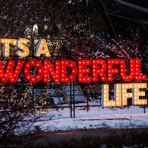 May include: A red and white illuminated sign with the words "It's a Wonderful Life" in a snowy outdoor setting.