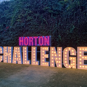 May include: Large white letters spelling out "Horton Challenge" with light bulbs illuminating each letter. The letters are on a green lawn in front of a dark green hedge.