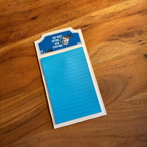 May include: A blue notepad with a white border and a white backing with the text "DO NOT drink the coffee." and a cartoon image of a coffee cup with the text "CONVERSATIONALLY FUTURISTIC" on it.