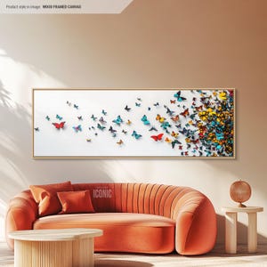 Puede incluir: Una impresión sobre lienzo rectangular larga con un fondo blanco y un diseño de mariposas coloridas volando en diagonal de izquierda a derecha. Las mariposas son de varios tonos de azul, verde, amarillo, naranja y rojo. El lienzo está enmarcado en un marco de madera delgado.