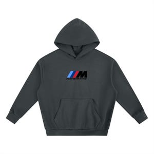 May include: A dark charcoal grey hooded sweatshirt featuring long sleeves, a front kangaroo pocket, and a hood. The centre of the chest displays the M Performance logo, consisting of three slanted stripes in light blue, dark blue, and red, followed by the letter M and the word PERFORMANCE in black.