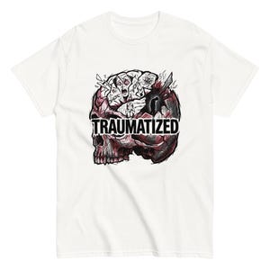 May include: White t-shirt featuring a graphic design of a skull with a brain and the word "TRAUMATIZED" in bold, black letters. The skull is red and black, with the brain in shades of gray and white.