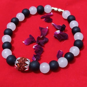 Peut inclure: Un bracelet composé de perles noires et blanches avec une perle en bois brun au centre. Le bracelet est sur un fond rouge.