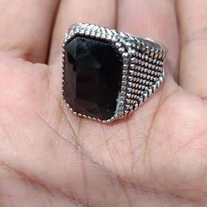 Op de afbeelding: Een zilveren ring met een grote, zwarte, rechthoekige edelsteen. De ring heeft een getextureerde band.
